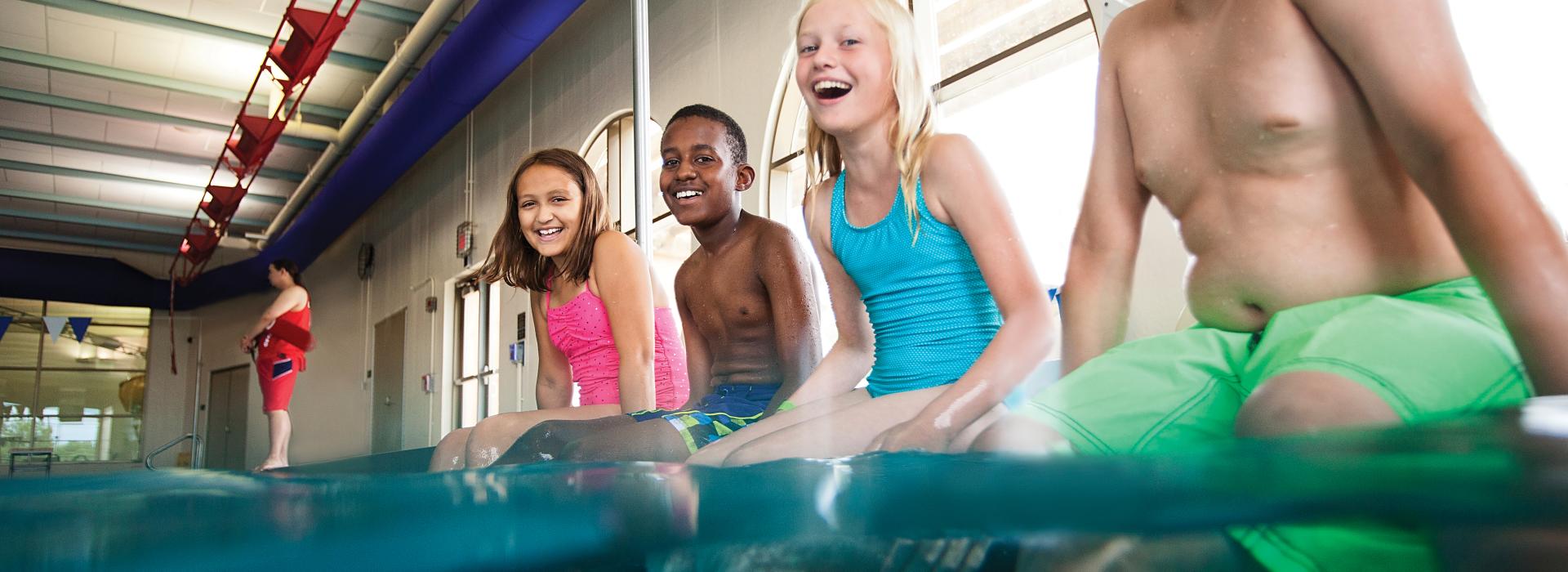 Kids sitting on the side of the pool with their legs in the water