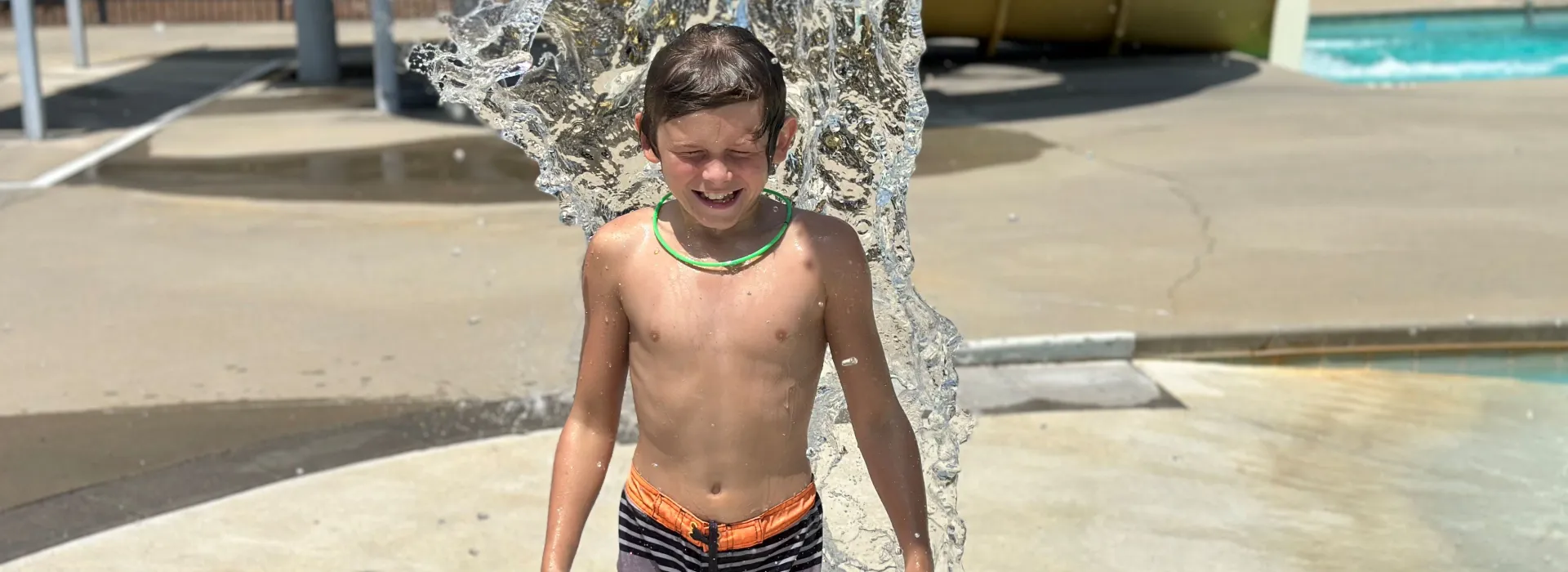 Boy under dump buckets at pool with a smile